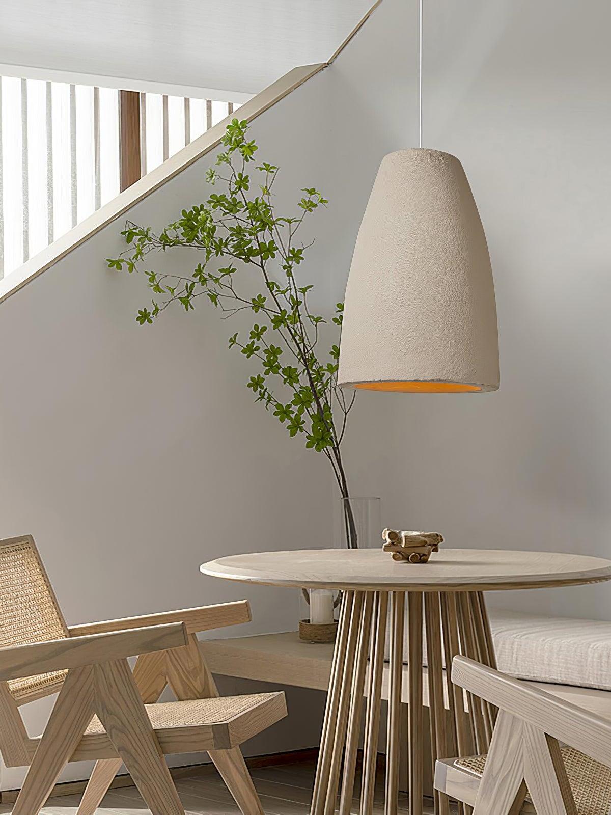 Tapered pendant above a round spoke-pedestal table with cane chairs, leafy vase and diagonal stair wall