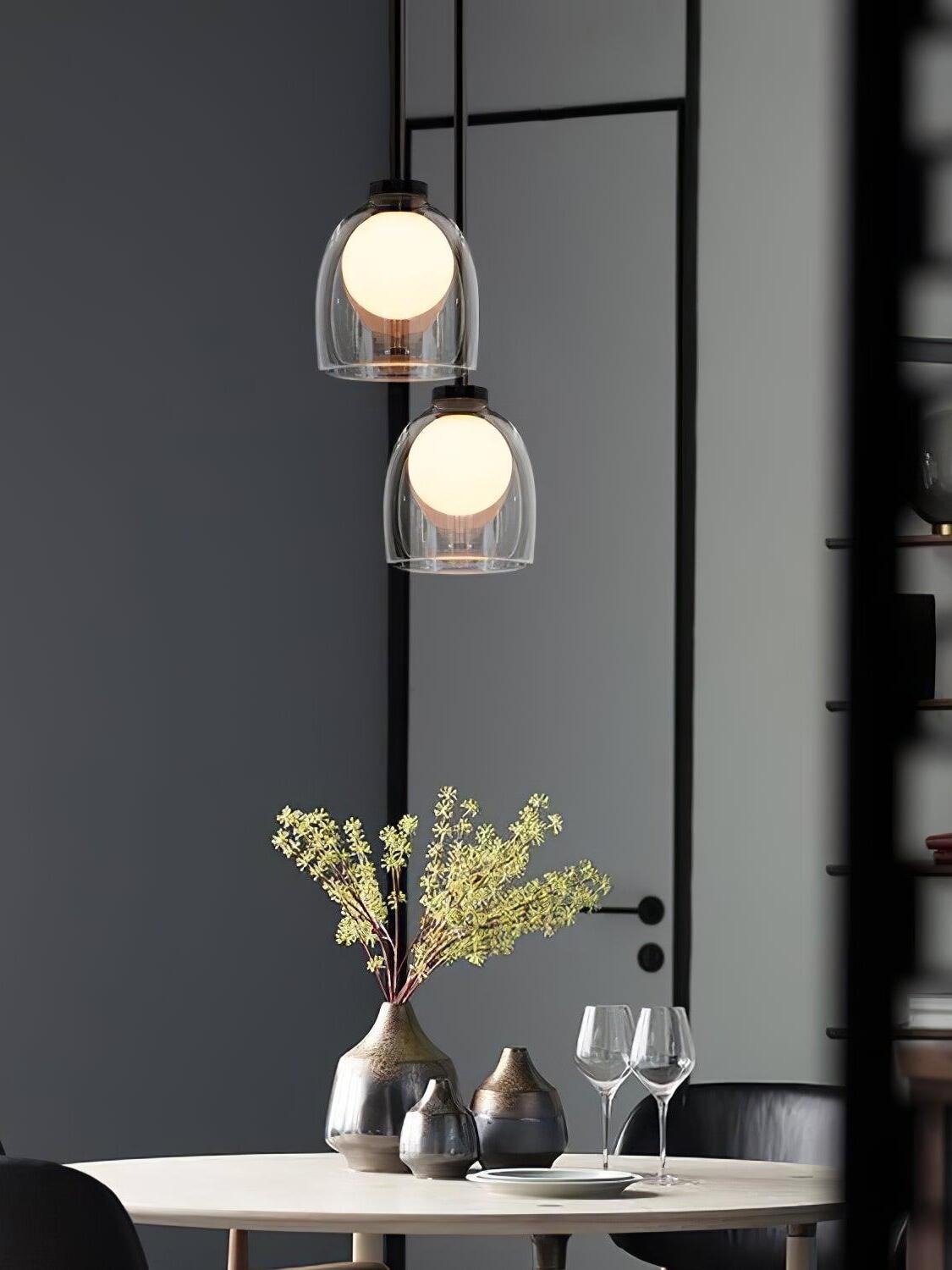 Two clear Crux glass pendants at different heights above a dining table with vases