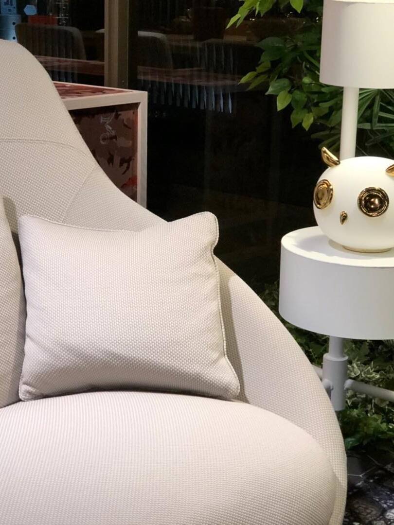 Owl on white circular side shelf beside upholstered chair and shaded lamp