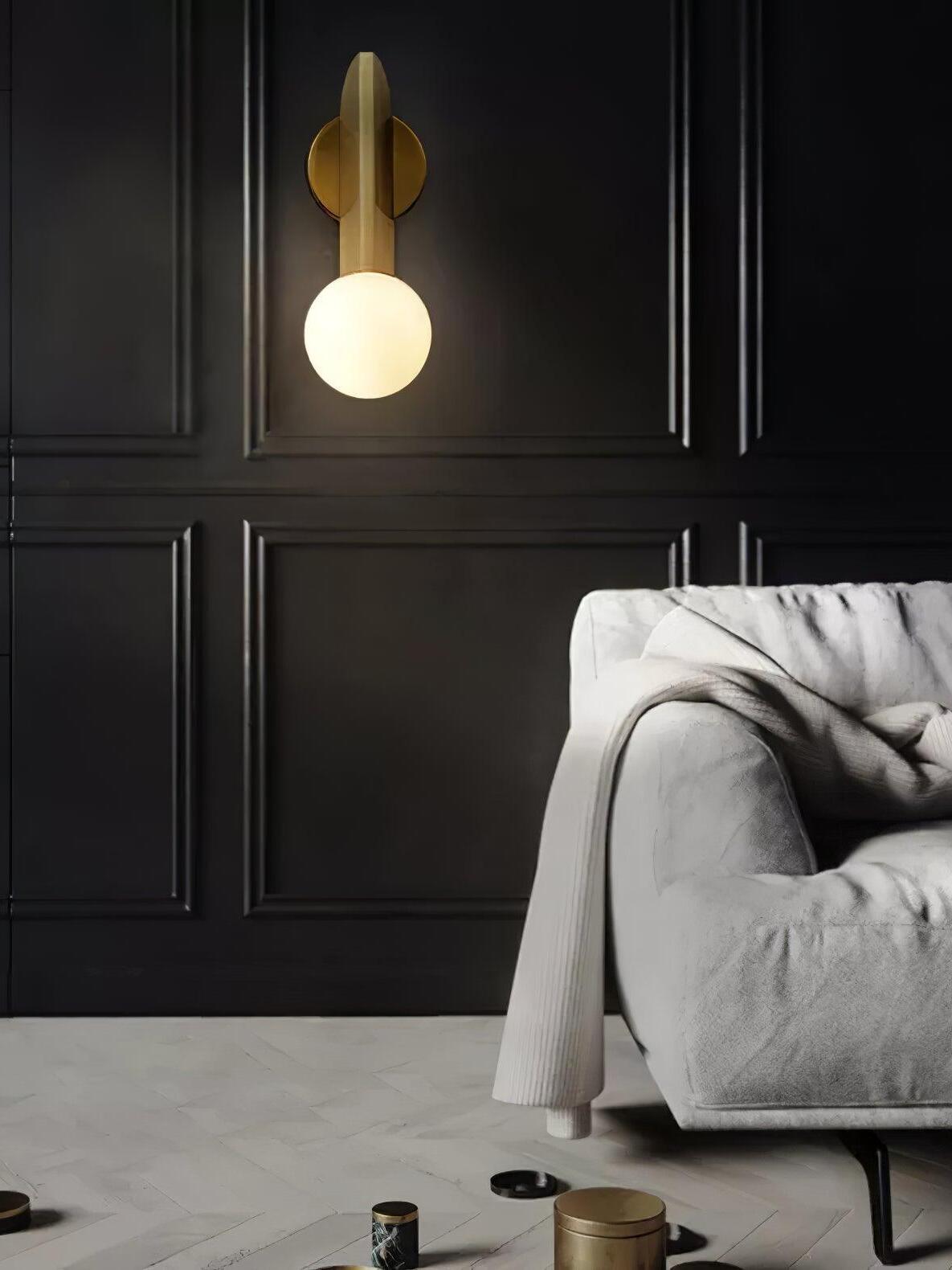 Globe-down wall lamp on a dark panelled wall beside a grey sofa, with a lit white sphere