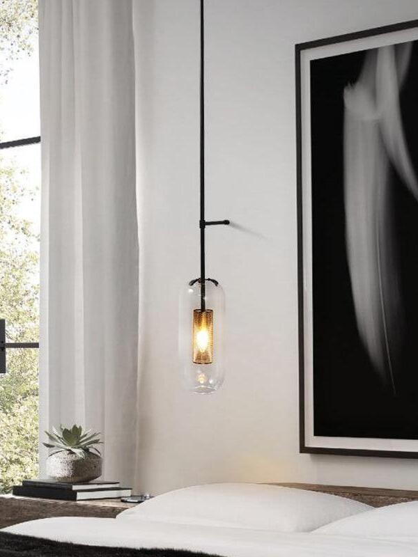 Black rod fixture with a lit glass capsule beside a bed, framed portrait and window curtains