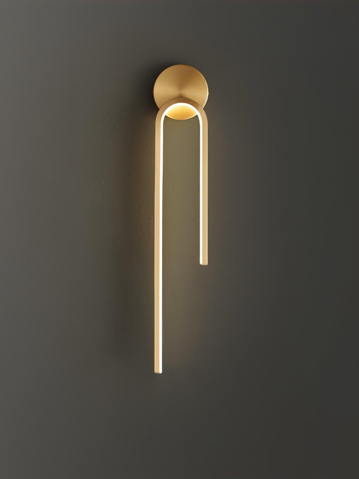 Gold-tone arch with a glowing inner strip, long left arm and round mount against a dark gray wall