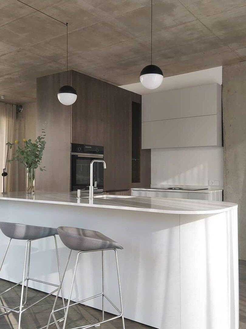 Two black-topped white globe pendants over a kitchen island and sink with grey stools and wood cabinets