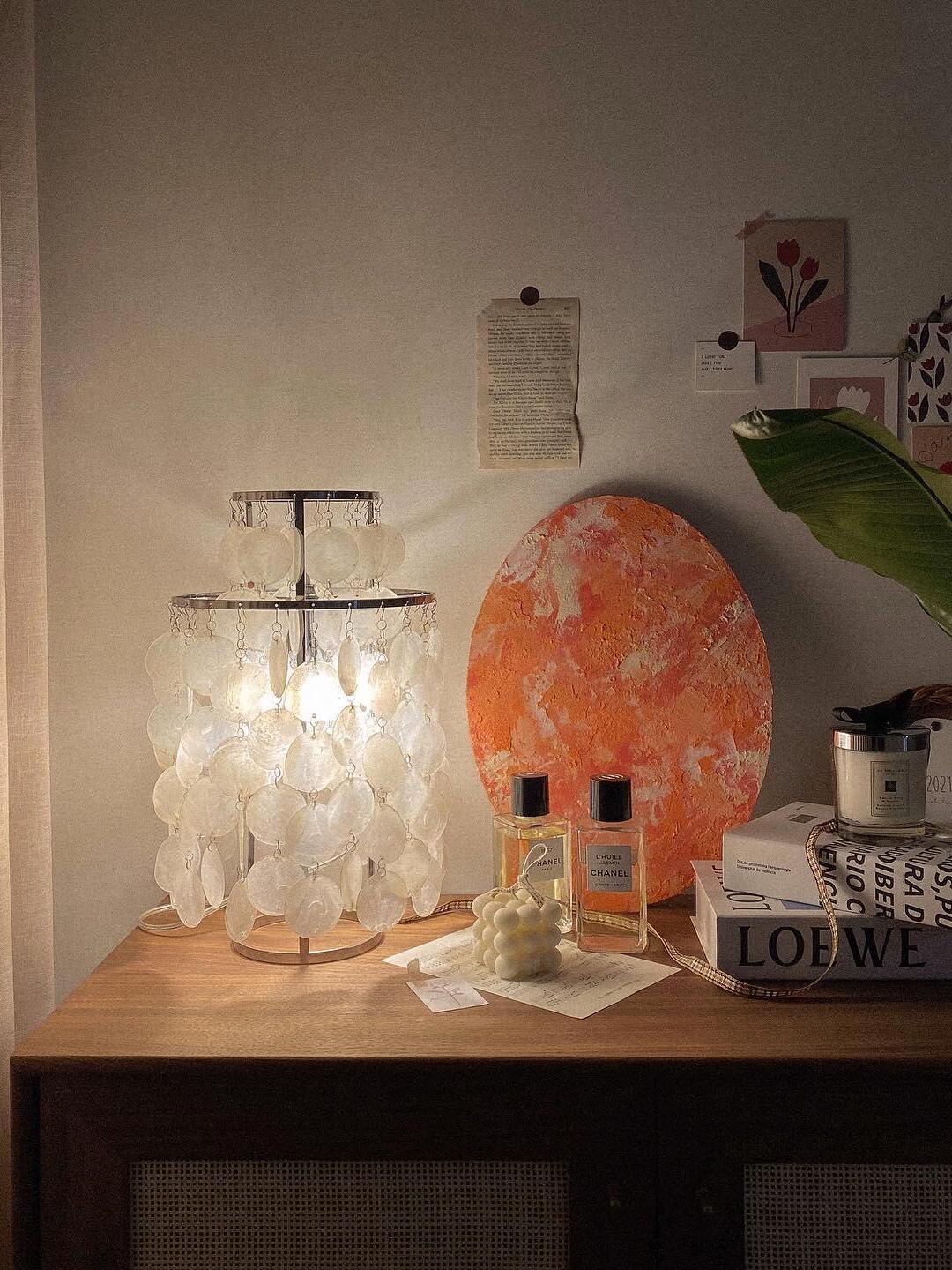 Shell lamp on wooden cabinet beside art and books