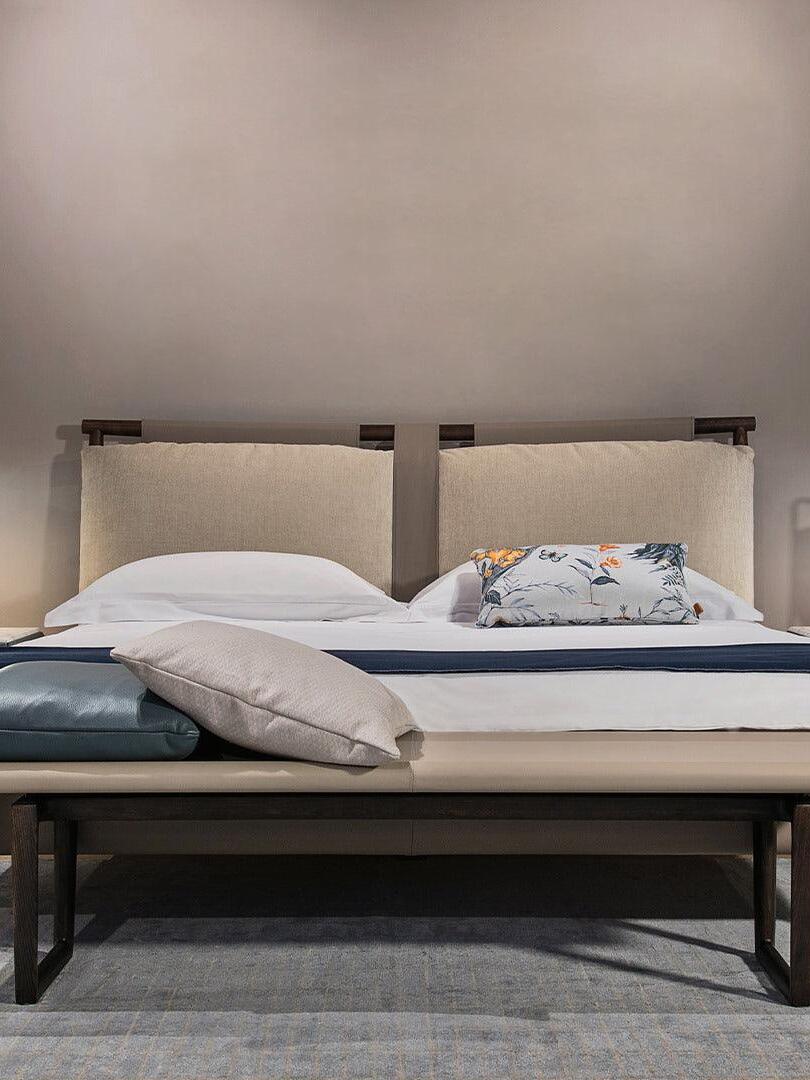 Bedroom with separate lamps flanking a padded bed, layered pillows and a bench at the foot