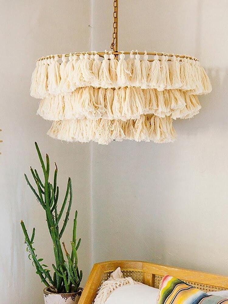 Cream-white tiered tassel chandelier above a cane seat beside a tall cactus and cushions