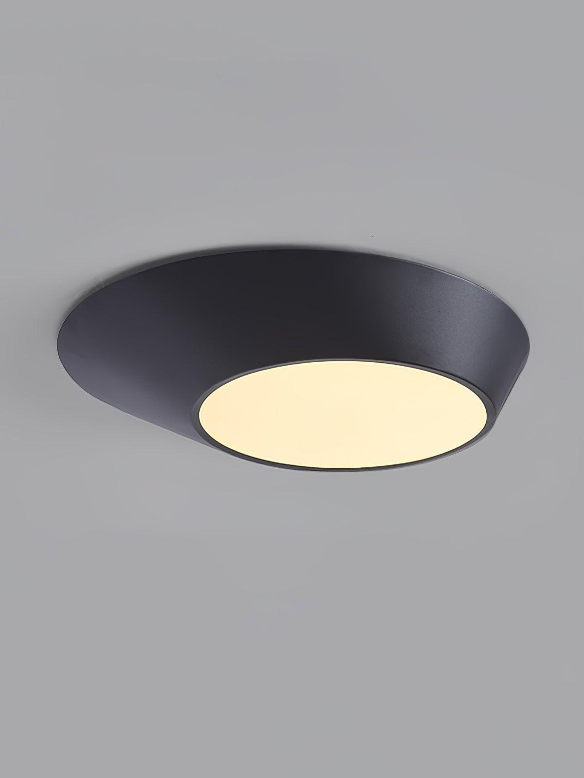 Black angled ceiling light with a warm-looking circular diffuser against gray