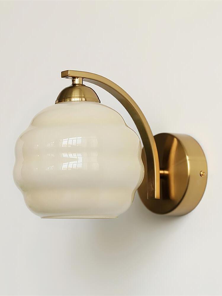 Pale beige contoured glass shade with gold-colored cap, curved arm and round wall plate on the right