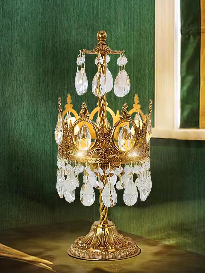 Illuminated crystal table lamp with upper drops against a green wall beside a picture frame.