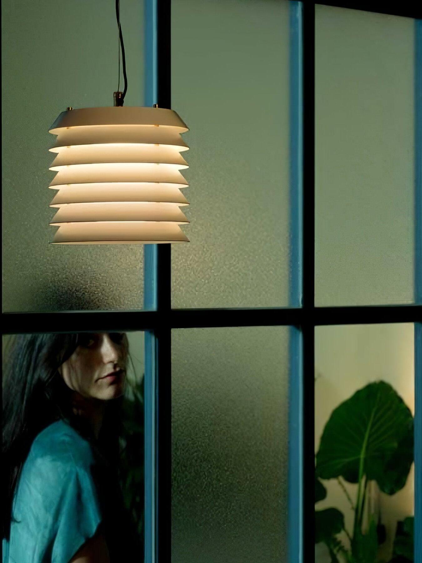 Lit pale layered pendant beside window with person and leaf below