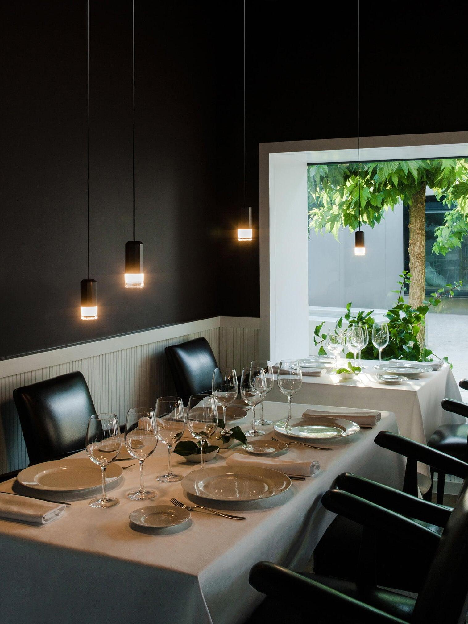 Lit pendant heads above a set dining table with glasses and a bright garden window