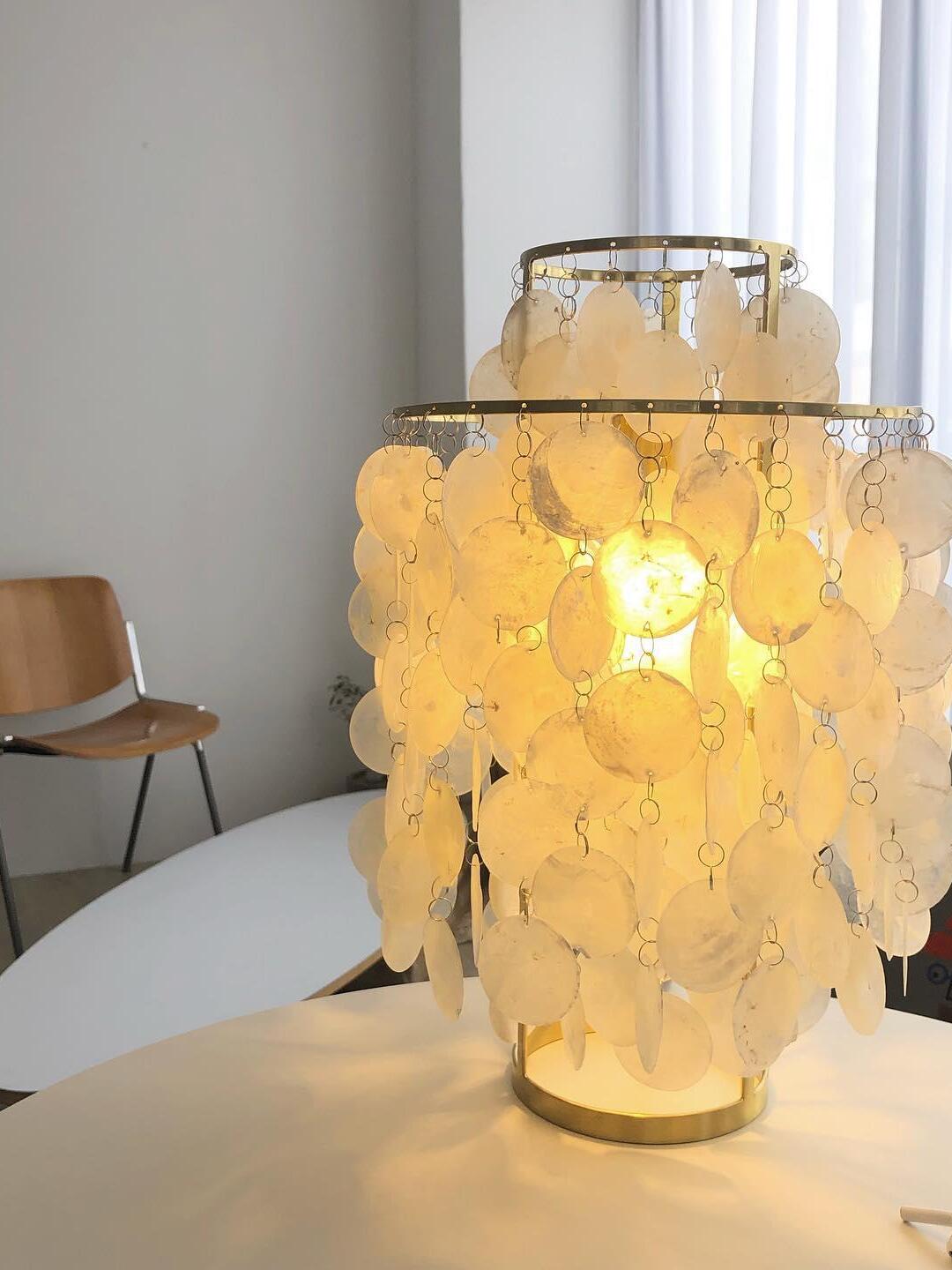 Lit shell table lamp on pale surface beside window