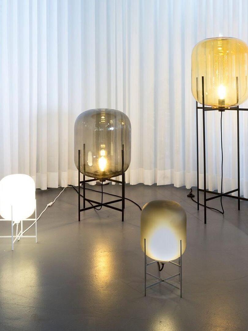 Glass lamps in several heights and colours arranged against pale curtains.