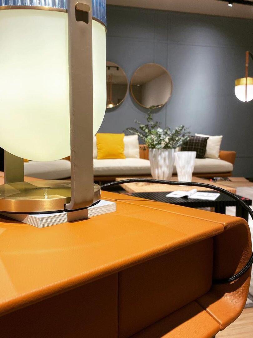 Cropped Xi lamp with gold-tone base and dark lead on an orange cabinet, with sofa and mirrors behind