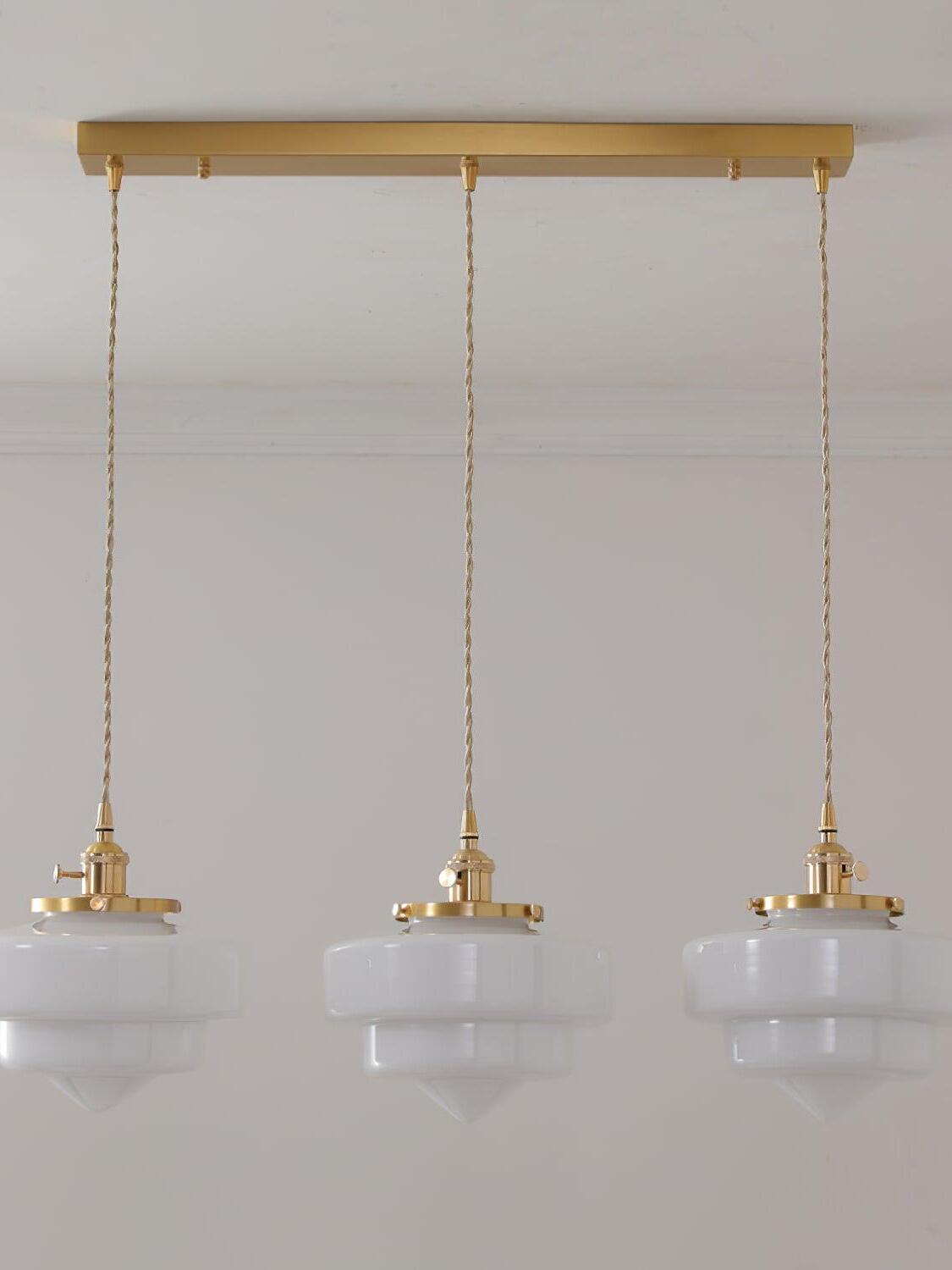 Front view of three unlit-looking Atlas Model A white glass shades beneath one long rectangular brass canopy