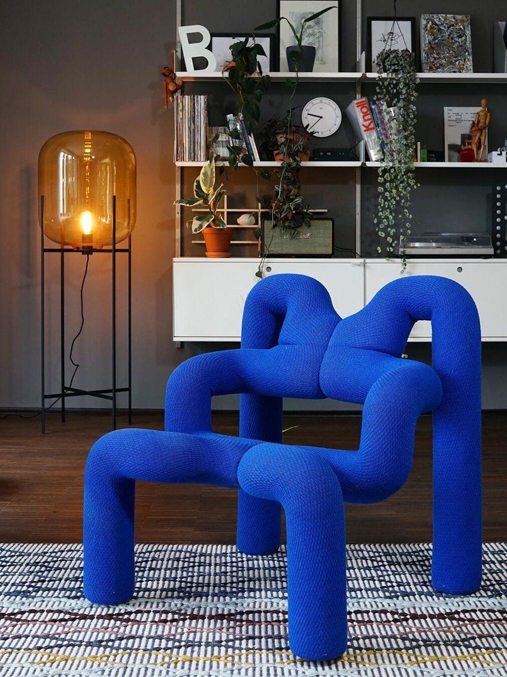 Illuminated amber floor lamp behind a sculptural blue lounge chair.