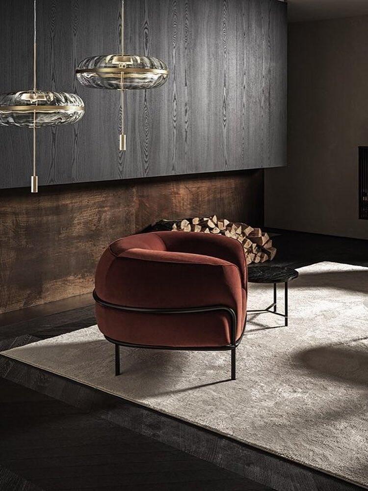 Two glass dome pendants above a rust-coloured lounge chair beside stacked firewood