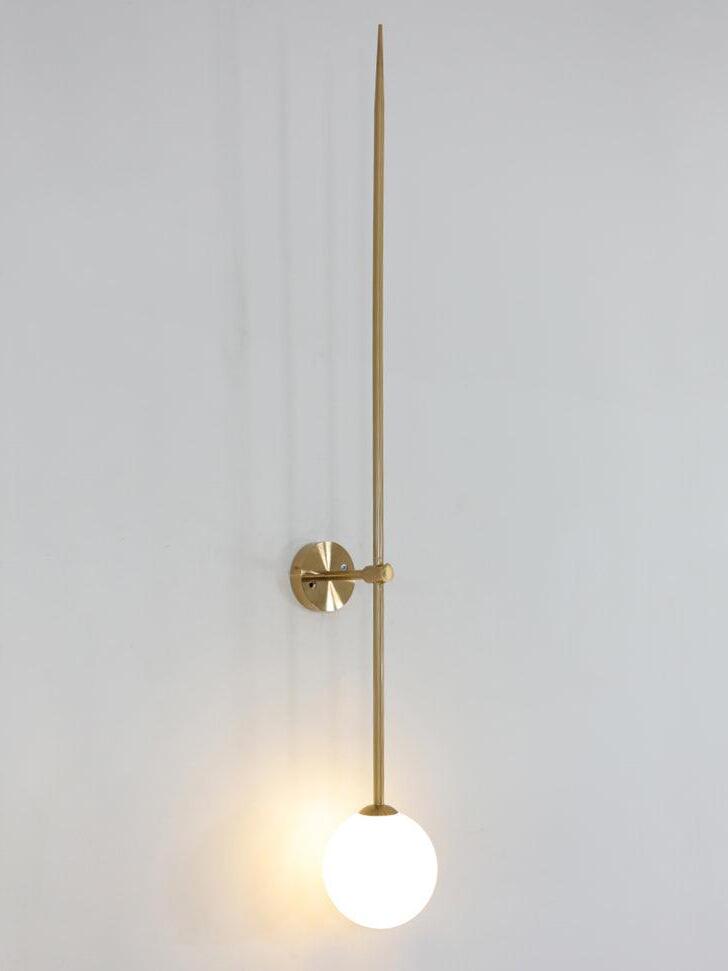 Angled lit gold-tone linear wall light with a white globe casting a warm-looking wall glow