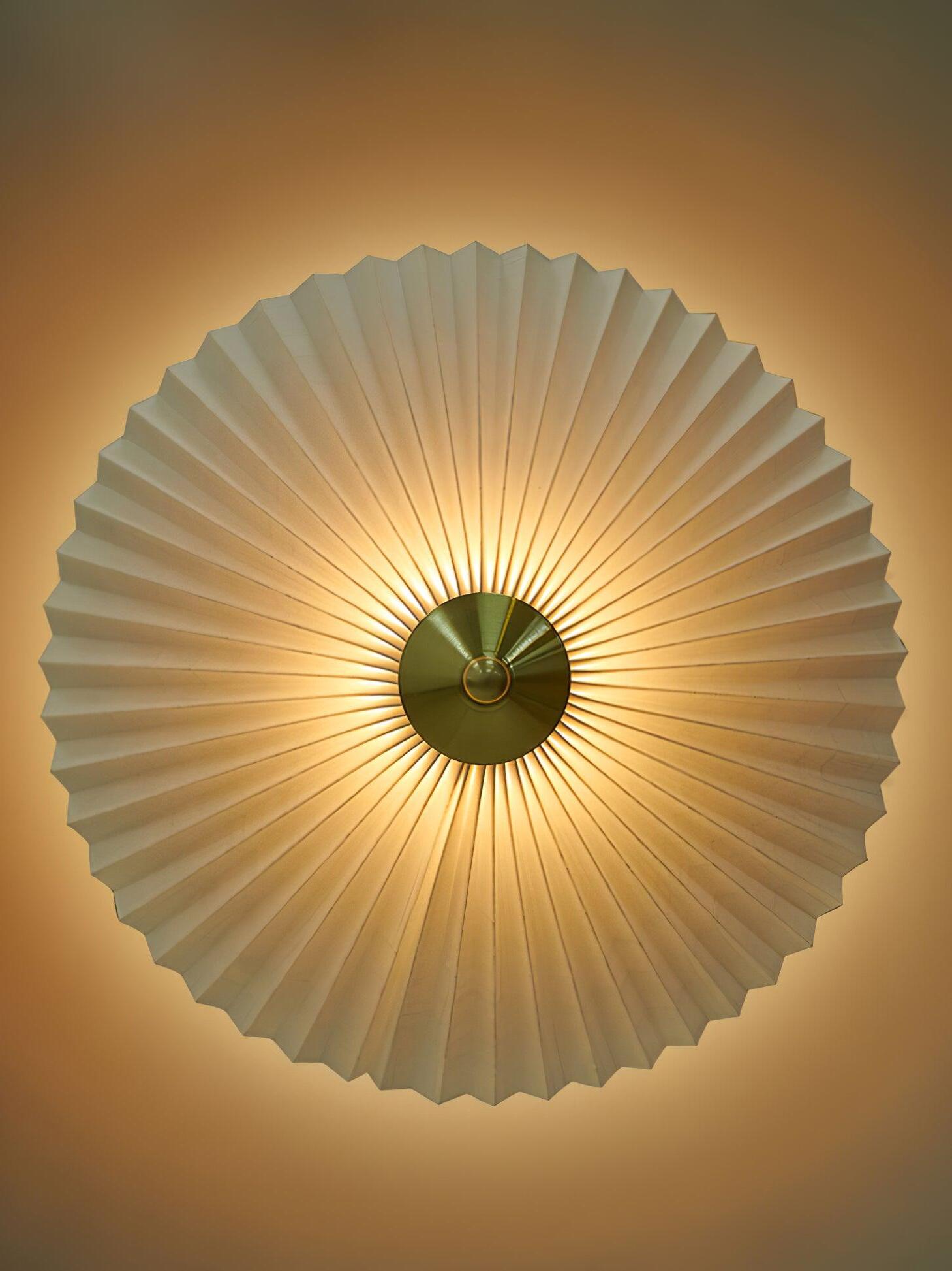 Overhead view of the radial pleats and central gold-tone cap of an illuminated shade