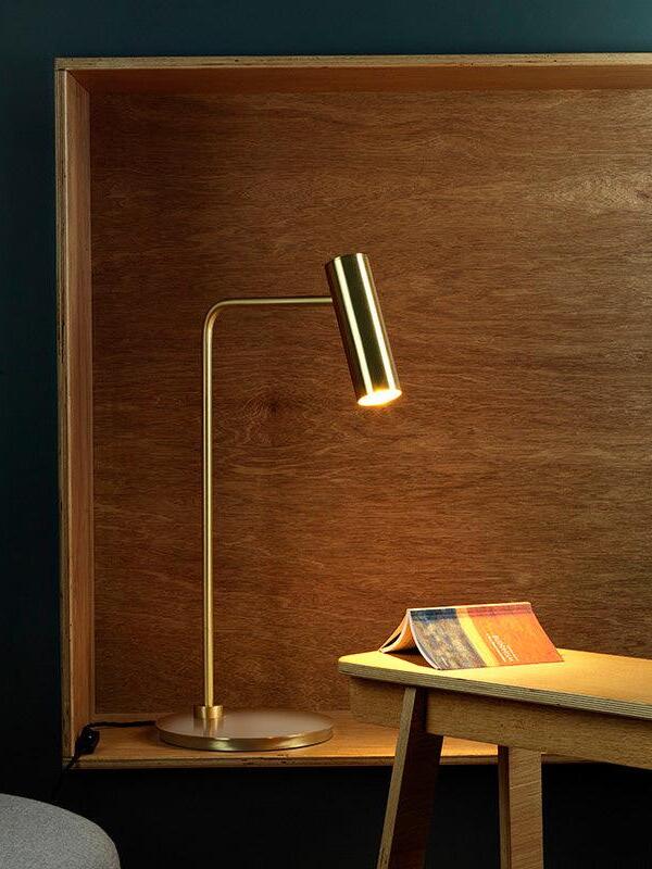 Lit gold-tone cylinder-head lamp near open book against wood panel