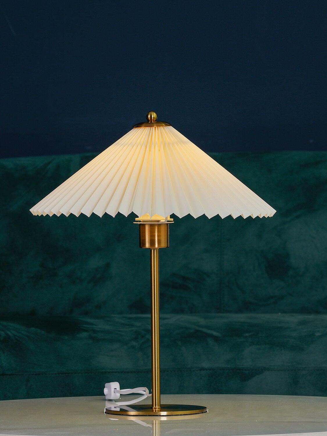 Perla lamp illuminated on the white table against a dark wall and green sofa