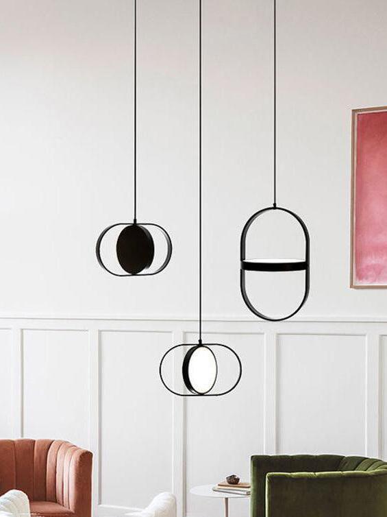 Three oval-frame disc pendants at different heights beside coral and green chairs in a paneled living room