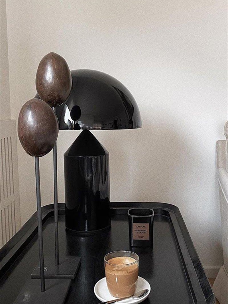 Glossy black mushroom lamp on a dark tray beside a candle, cup and oval decorative objects