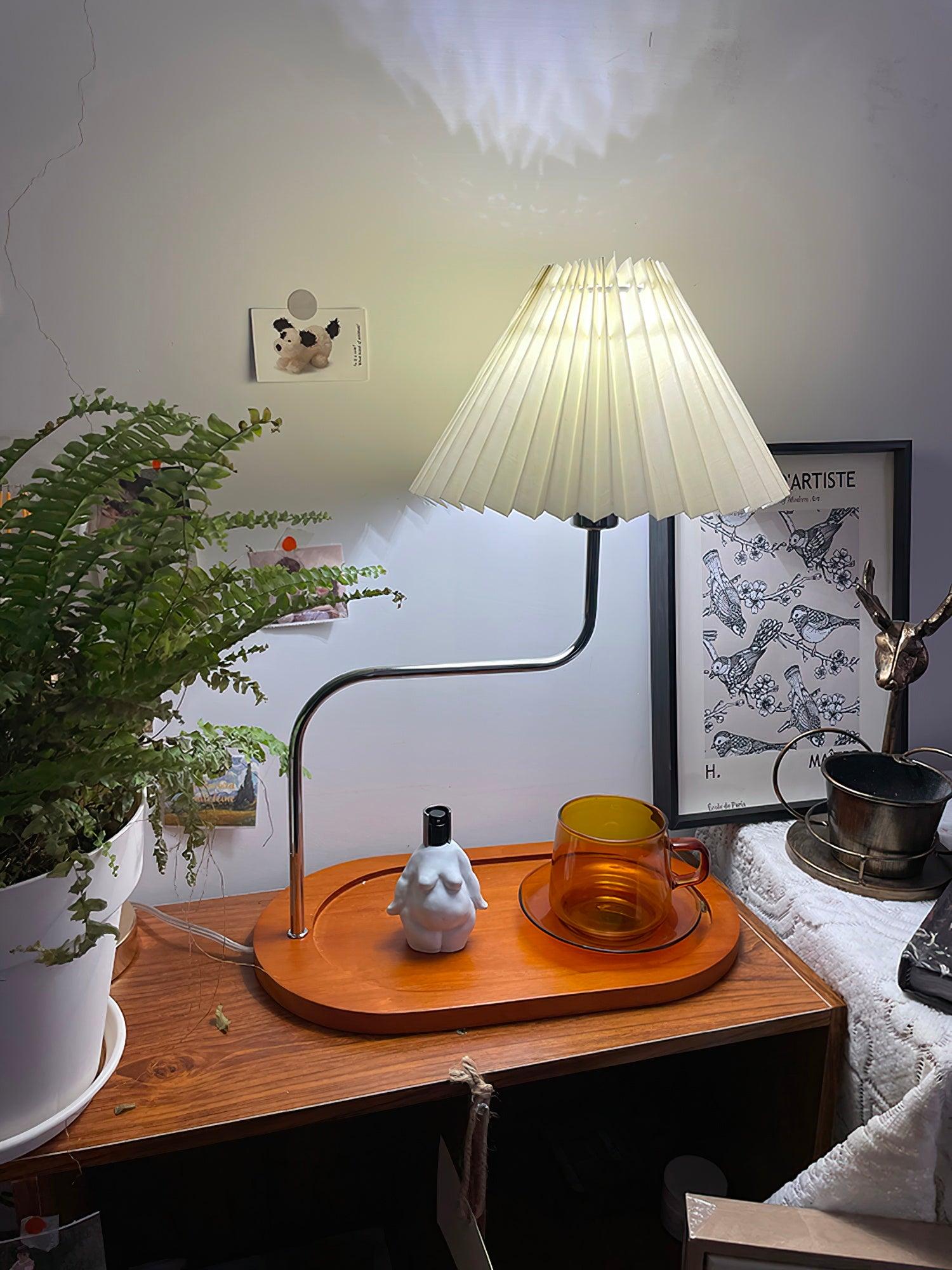Lit table lamp on wooden tray beside coloured glass