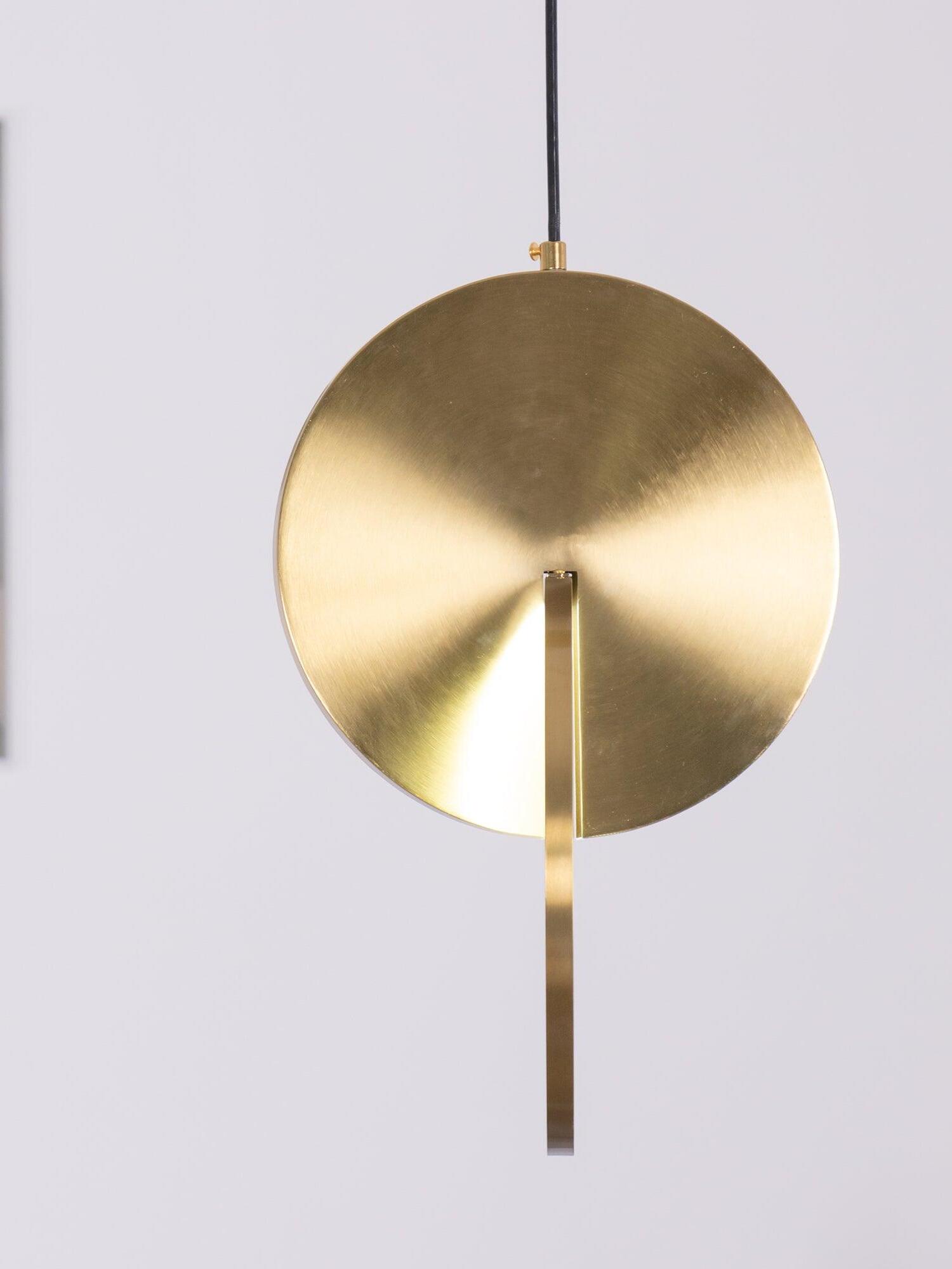 Near edge-on view of a gold disc pendant showing the metal face, narrow diffuser rim and black cord