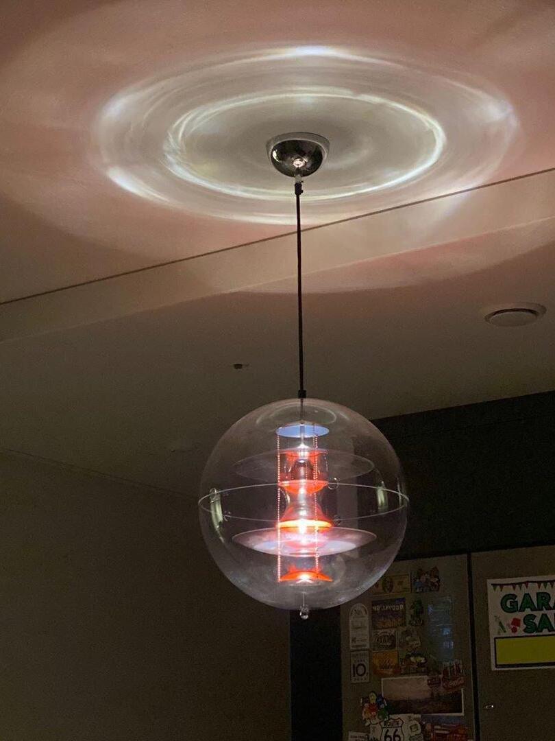 Clear globe pendant on a black cord beneath a chrome-tone canopy, with a circular light reflection on the ceiling