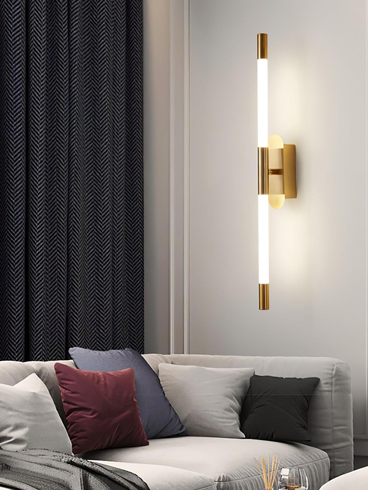 Vertical gold Agnes wall light above a sofa with dark curtains and cushions