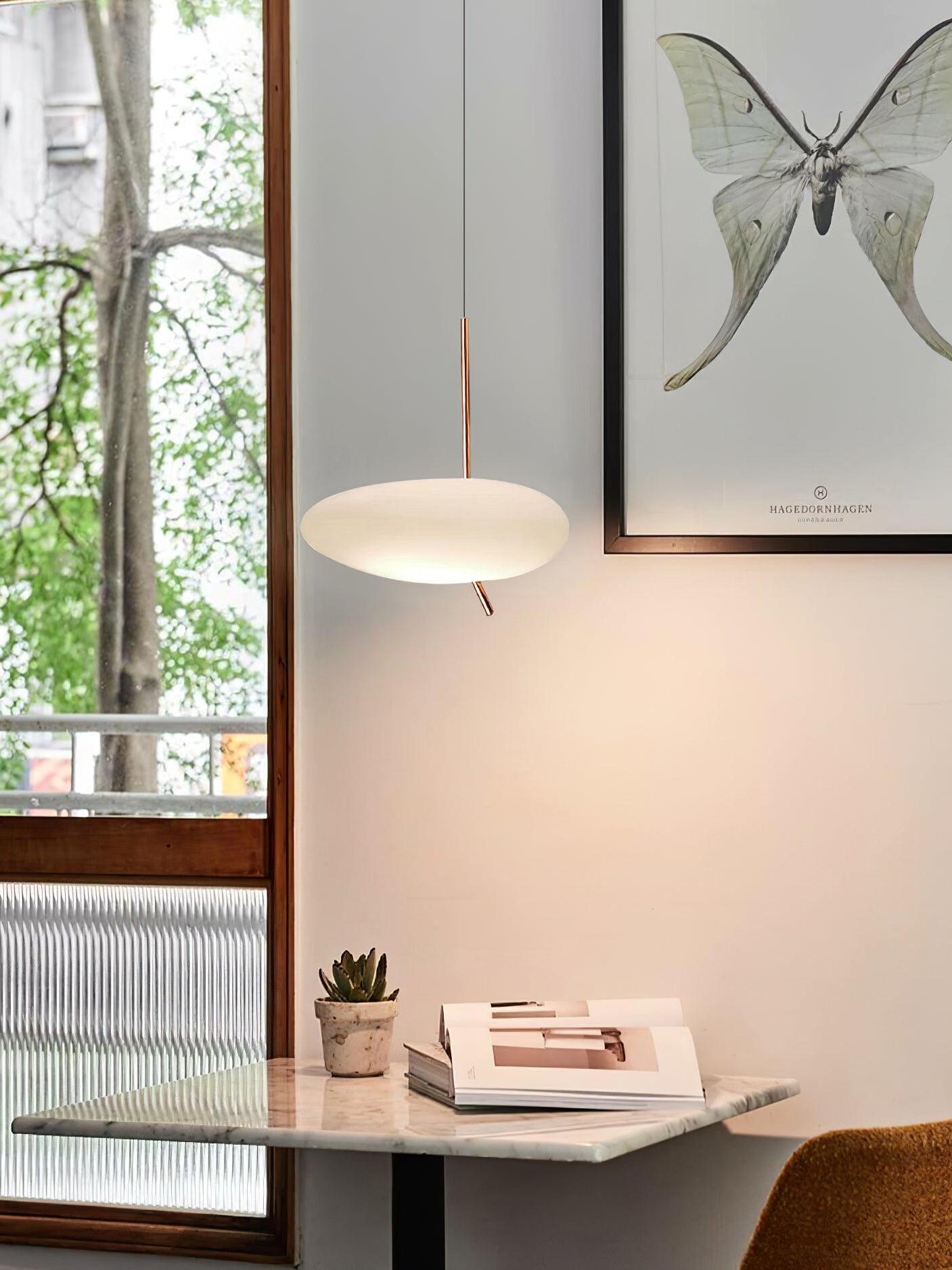 White pendant beside a window, framed butterfly artwork and books on a console