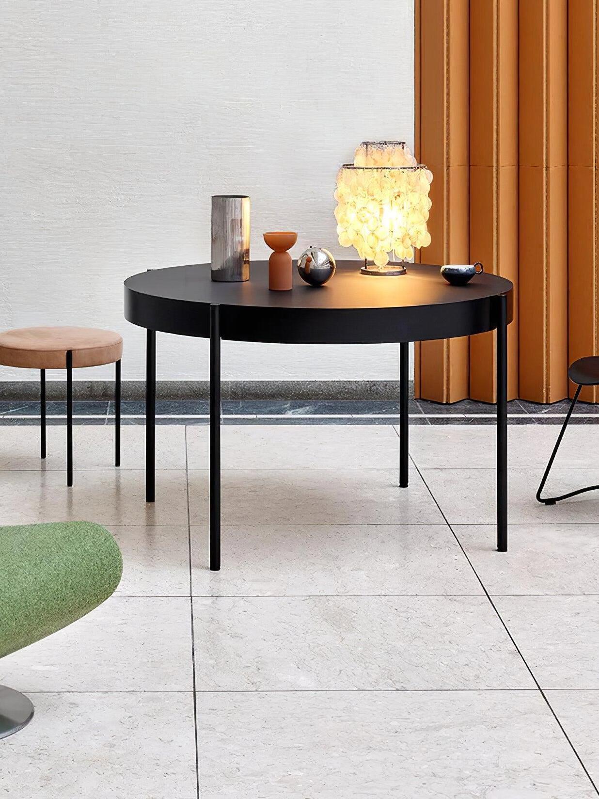 Lit shell table lamp on black table beside orange curtain