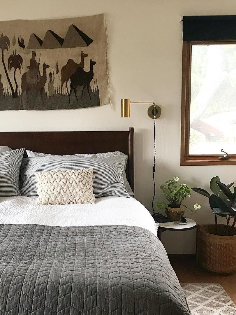 Brass-tone light beside grey-covered bed and leafy plants