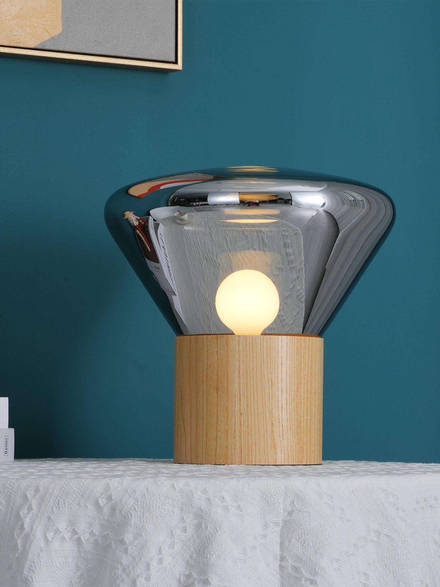 Smoky glass shade around round lit bulb on wood base against teal wall