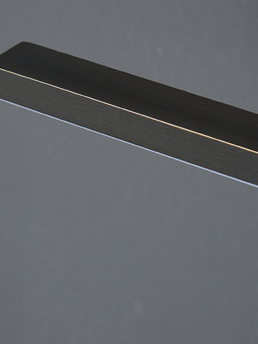 Close-up of black linear light bar end with pale underside strip, dark brushed surface and thin gold-tone edge