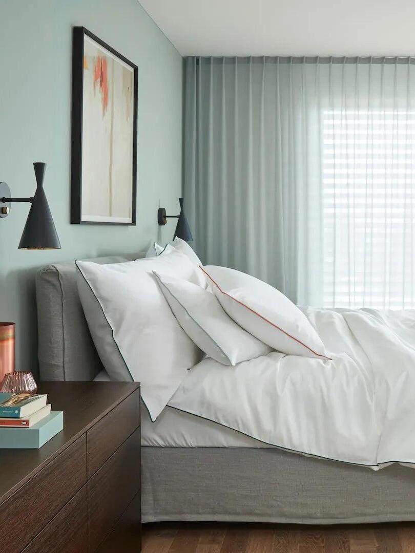 Black Beat wall sconce by a pale bed and grey curtains