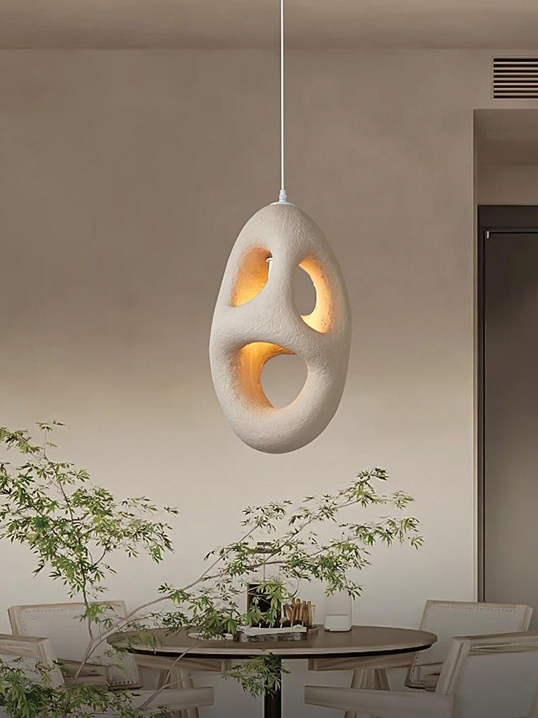 Lit three-opening sculptural pendant above a round dining table with pale chairs and a Green branch arrangement