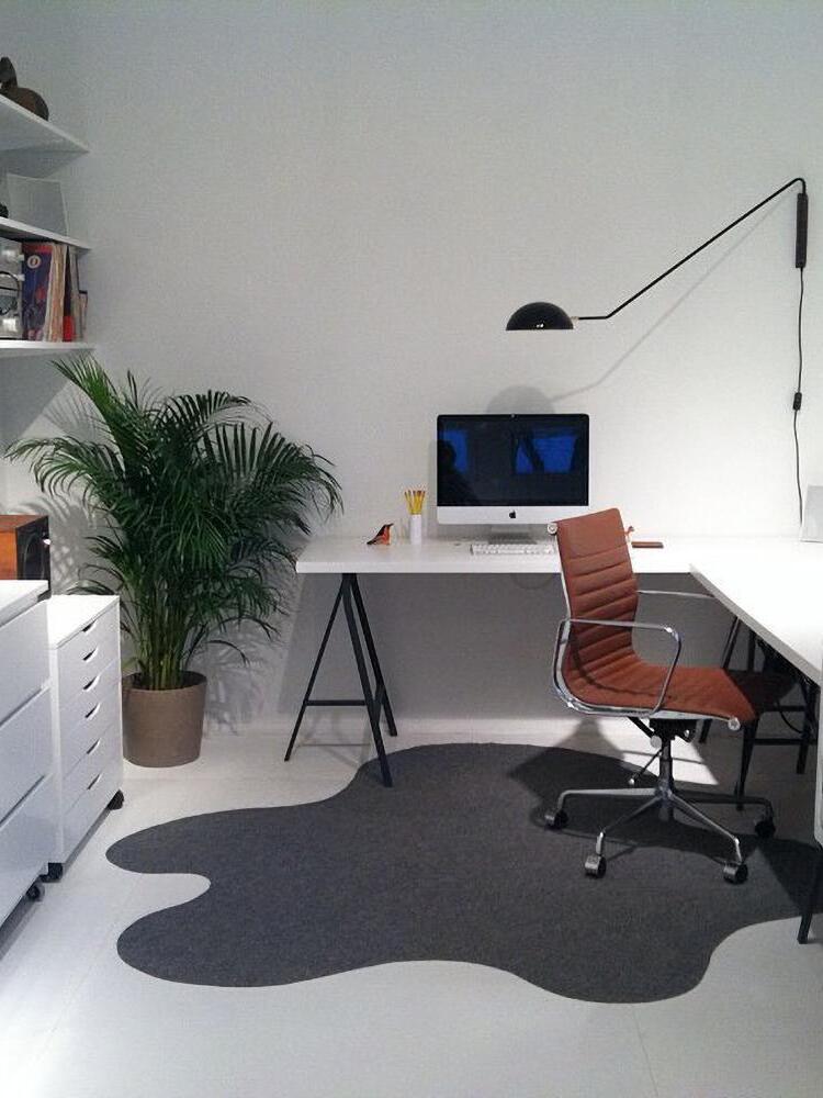 Black long-arm wall lamp over a white office desk and computer, with wooden wall mount, switched cord and brown chair