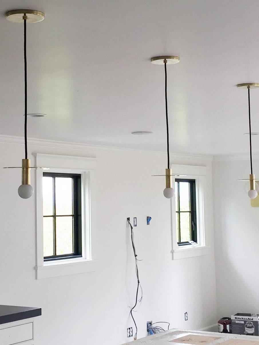Three brass-tone disc pendants with separate canopies in a white room with black window frames