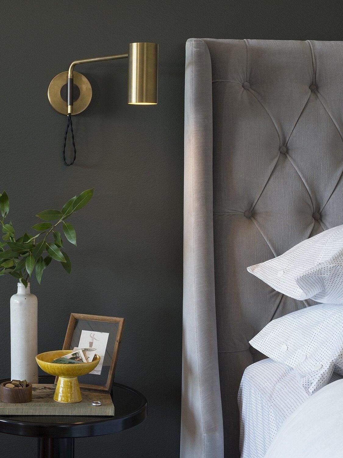 Brass-tone wall light beside grey upholstered headboard