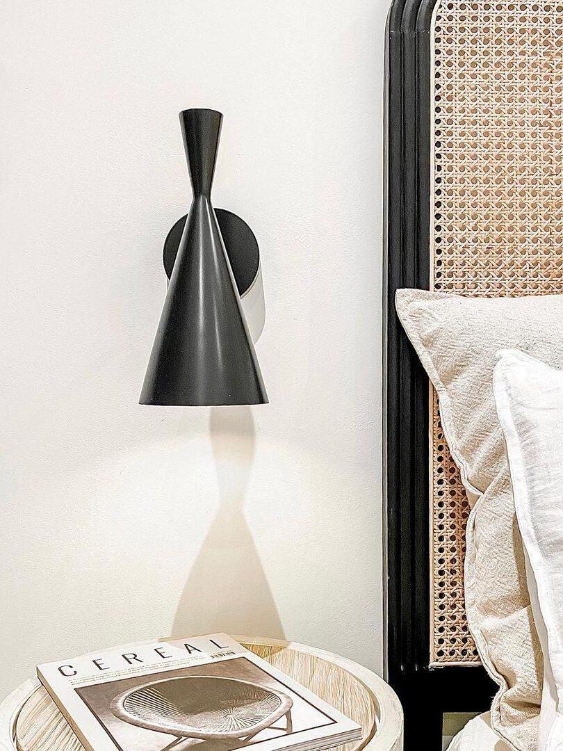 Black cone wall lamp over bedside books