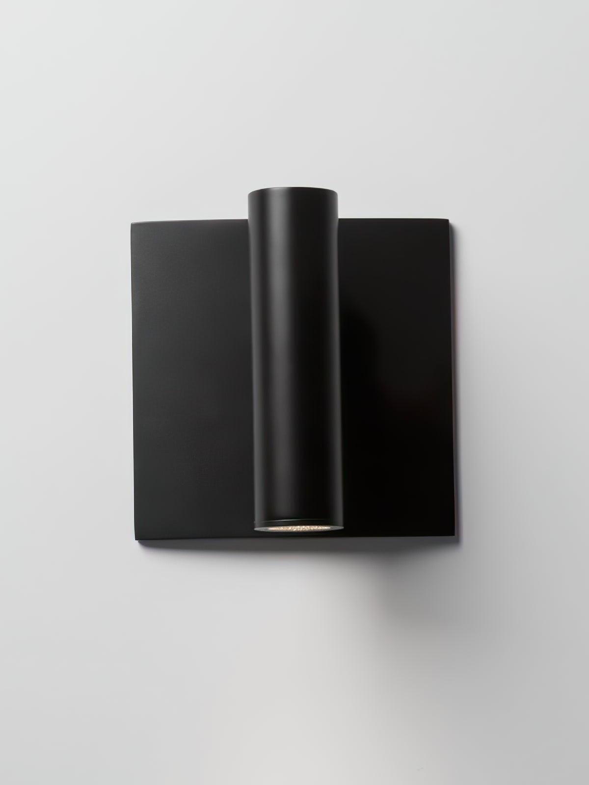 Front view of black Enna wall light with vertical cylindrical head and square plate against pale background