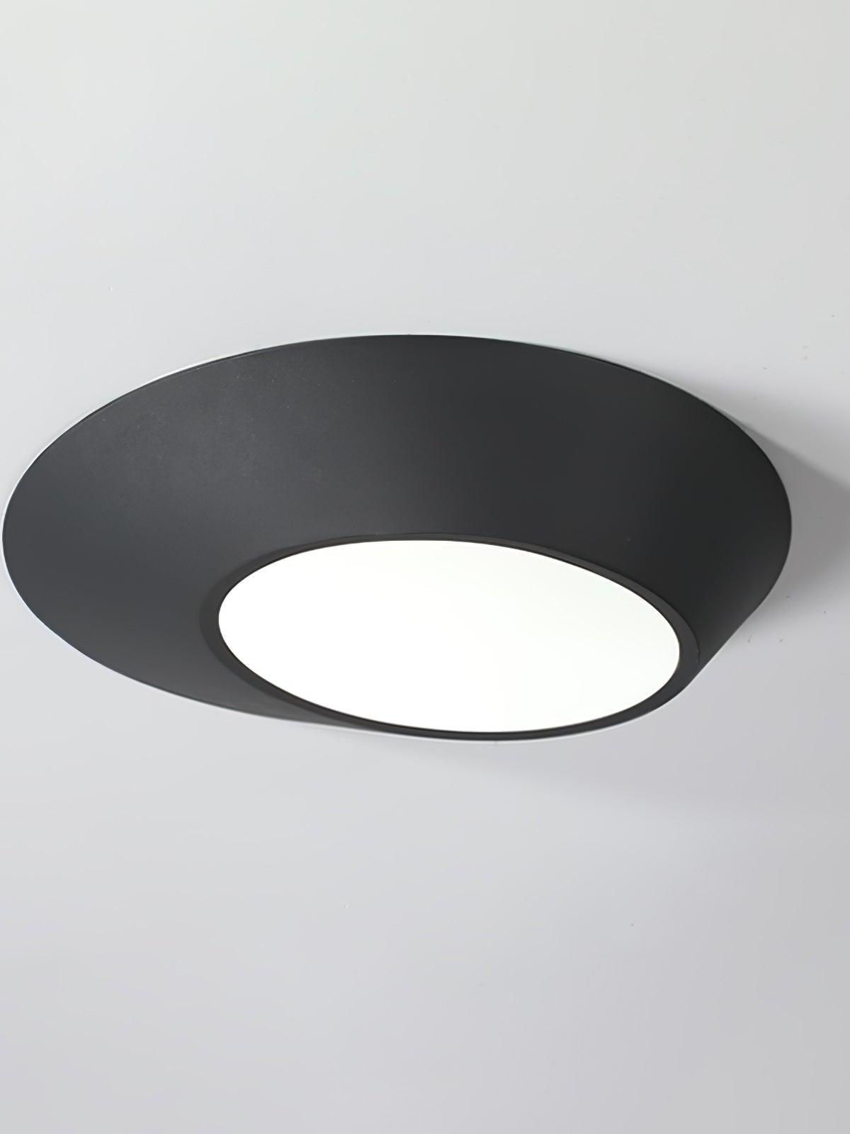 Black angled round ceiling light with a white-looking glowing diffuser against a pale ceiling