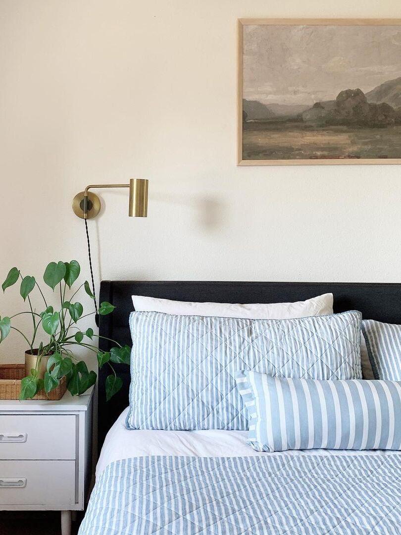 Brass-tone cylinder light beside black headboard and white pillows