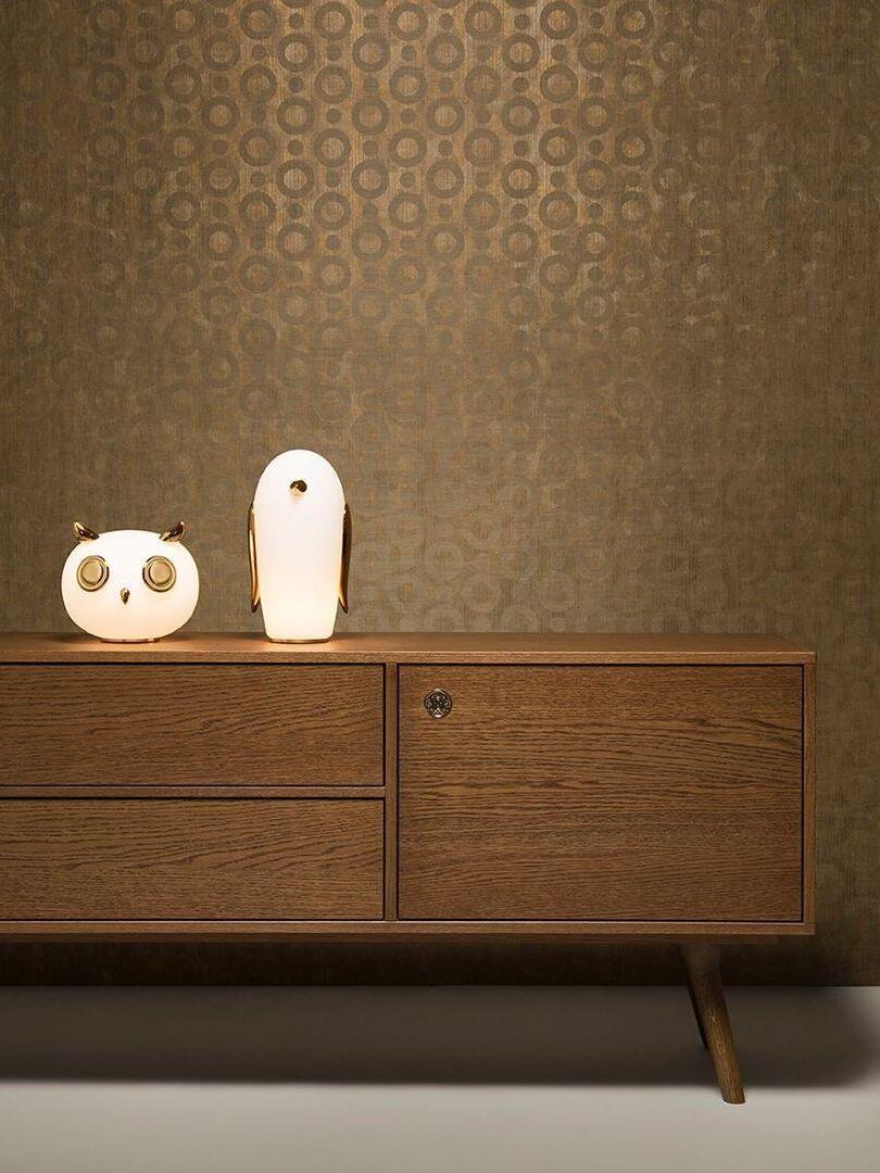 Owl and penguin on wood sideboard against gold-patterned wallpaper