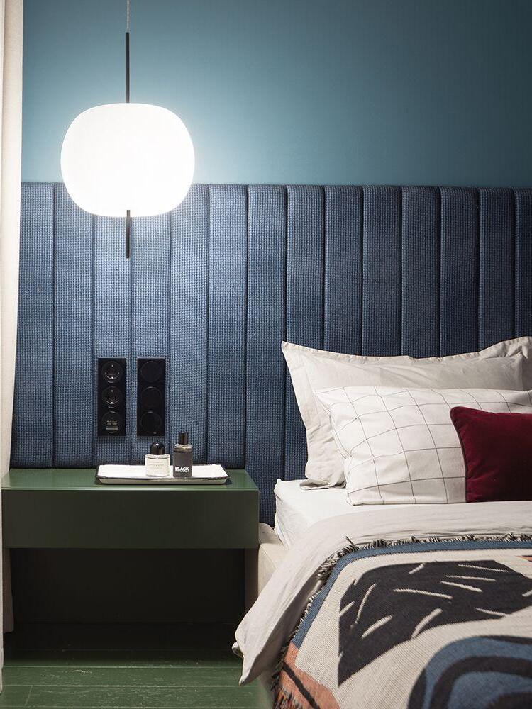Glowing white pendant beside a dark upholstered headboard