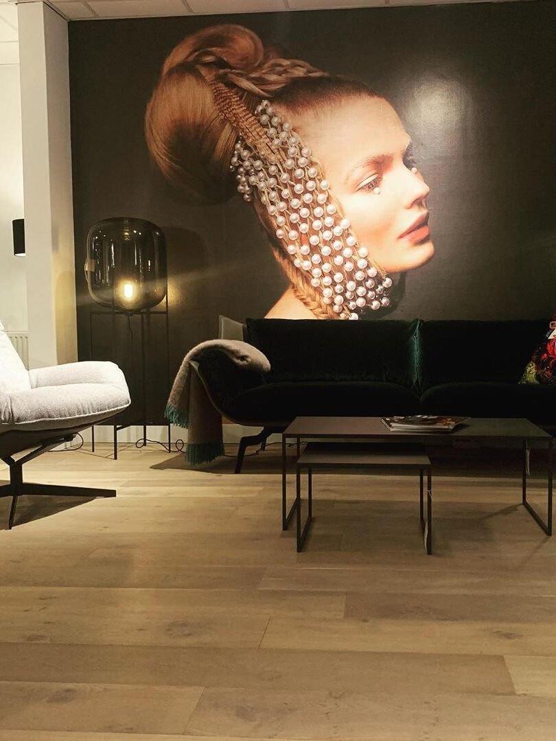 Low glass lamp beside a black sofa beneath a large portrait.
