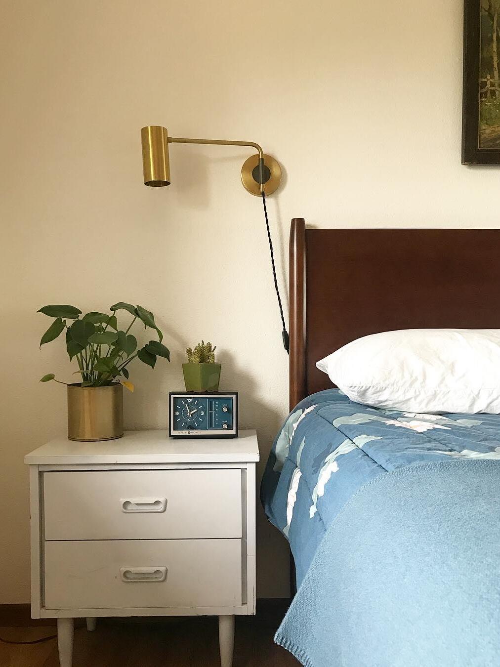 Brass-tone light above pale bedside cabinet and blue bedding
