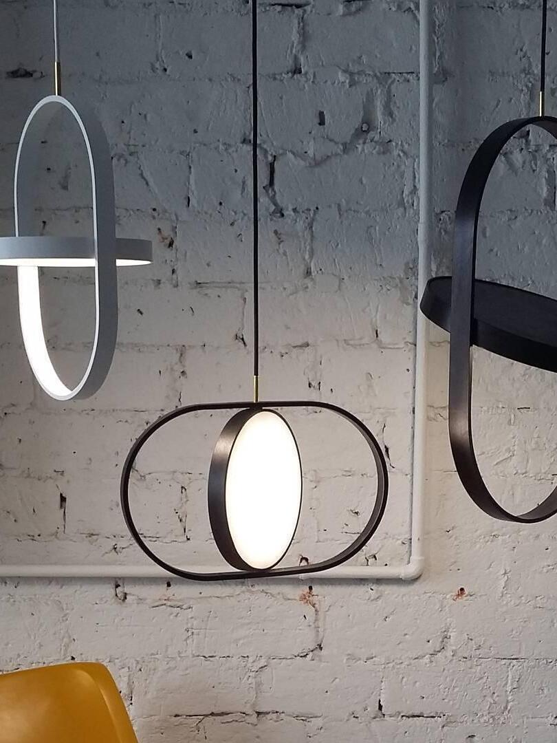 Gray and black oval-frame pendants with discs at different angles against a textured brick wall